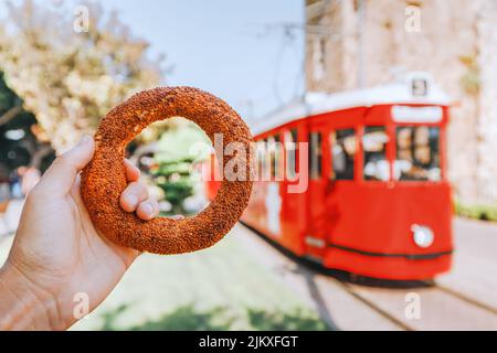 En-cas traditionnel de rue de bagel de Simit à l'arrière-plan du tramway rétro rouge dans la vieille ville d'Antalya, Turquie. Concept de voyage et de cuisine Banque D'Images