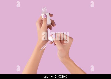 Les femmes tiennent main compte-gouttes avec du sérum sur fond de lavande pastel Banque D'Images