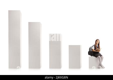 Écolière assise sur la première colonne d'un graphique à barres avec un livre dans ses mains isolé sur fond blanc Banque D'Images