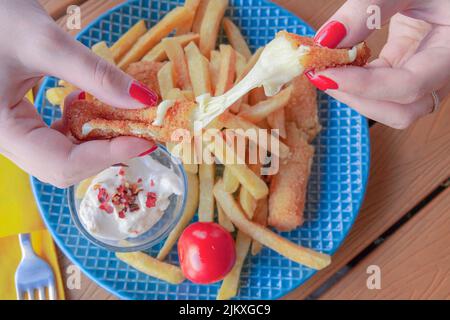 A closeup of the woman's hands holding Mozzarella sticks with French fries. Top view. Stock Photo