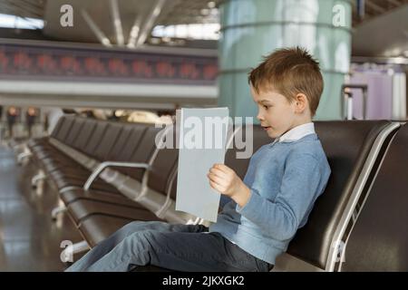 Un petit garçon lit un livre dans la salle d'attente de l'aéroport avant le vol Banque D'Images