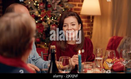 Belle femme discutant avec une femme âgée tout en appréciant le dîner de Noël à la maison. Les membres de la famille festive mangent des plats traditionnels faits maison tout en célébrant les vacances d'hiver. Cliché sur trépied Banque D'Images