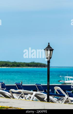 Foyer sélectif d'une lampe solitaire avec son ampoule éteinte pendant la journée dans une plage des Caraïbes, il ya quelques chaises longues de plage en arrière-plan, la mer Banque D'Images