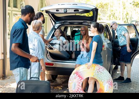 Petit enfant voyageant en vacances en famille, se préparant à aller en vacances au bord de la mer pendant l'été. Des personnes et des amis variés chargent la valise et le chariot dans le coffre de voiture, laissant sur le voyage. Banque D'Images