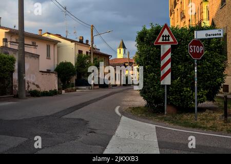 Rue dans la périphérie d'une ville italienne avec un panneau et une traversée de chemin de fer dans le fond au coucher du soleil Banque D'Images