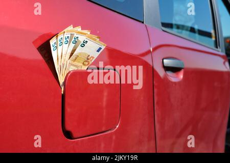 Cinquante billets de banque en euros qui sortent d'un réservoir fermé, prix élevé du carburant, argent devant une voiture rouge. Banque D'Images