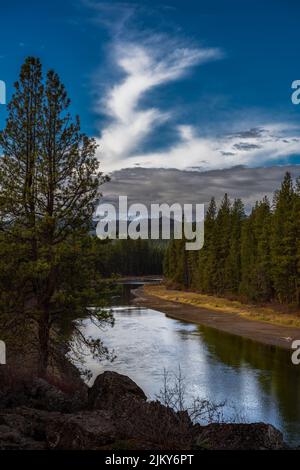 THE LOWER DESCHUTES RIVER LINED WITH TREES AND A BEAUTIFUL REFLECTION IN THE RIVER AND A CLOUDY SKY AND MOUNT HOOD NEAR SUNRIVER OREGON Stock Photo