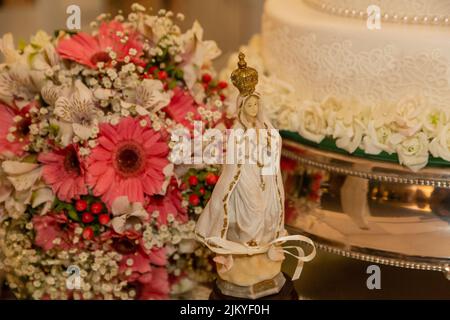 La statue de notre Dame de Fatima devant un bouquet de fleurs et un gâteau de mariage Banque D'Images