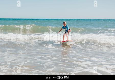 Enfants jouant et surfant sur la plage en petites vagues. Grands-mères regardant les enfants jouer. Enfants jouant sur un radeau dans les vagues. Les enfants attrapent la vague Banque D'Images