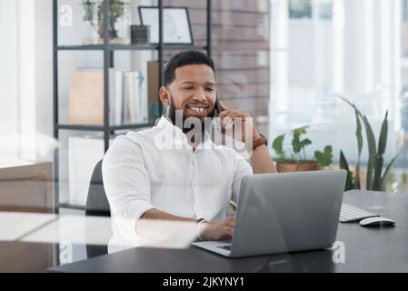 Je l'ai fait et je vais vous l'envoyer maintenant. Un jeune homme d'affaires parle sur un téléphone portable tout en travaillant sur un ordinateur portable dans un bureau. Banque D'Images