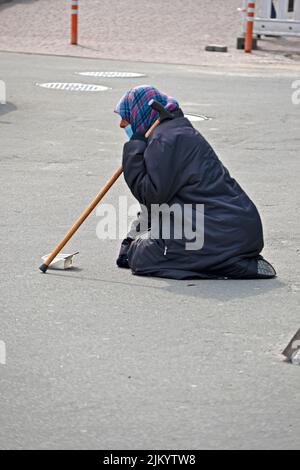 Une grand-mère âgée avec un foulard rayé et un bâton en costume noir, assise sur ses genoux, a chassés et a demandé de l'aide à Kiev, en Ukraine. Banque D'Images