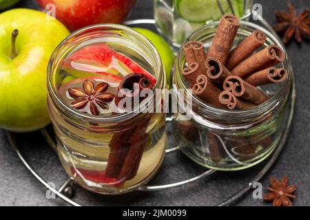 Bâtonnets de cannelle dans un pot en verre. Eau infusée à la cannelle et à la pomme dans un pot en verre. Pommes sur table. Gros plan. Arrière-plan noir. Vue de dessus Banque D'Images