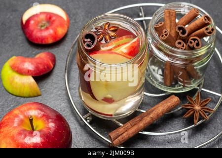 Eau infusée à la cannelle et à la pomme dans un pot en verre. Bâtonnets de cannelle dans un pot en verre. Pommes rouges sur la table. Arrière-plan noir. Vue de dessus Banque D'Images