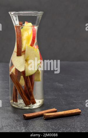 Eau infusée à la cannelle et à la pomme dans une bouteille en verre. Bâtons de cannelle sur la table. Copier l'espace. Arrière-plan noir. Banque D'Images
