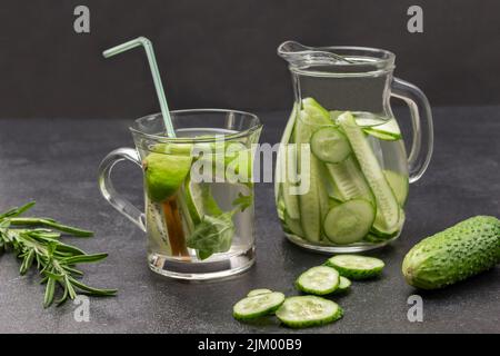 Eau infusée au kiwi et à la chaux dans du verre. Eau perfusée au concombre dans une verseuse en verre. Branche de romarin et de concombre sur la table. Arrière-plan noir. Banque D'Images
