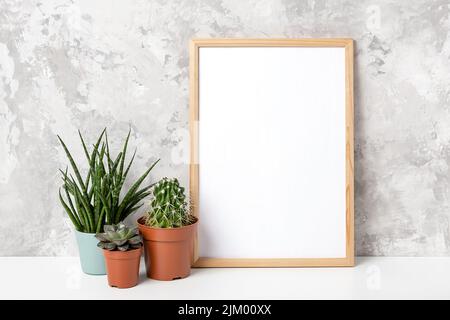Cadre vertical en bois avec carte blanche vierge, et fleurs vertes de la maison en pot sur table sur fond de mur en béton gris. Modèle de maquette pour votre Banque D'Images