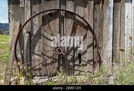 Roue en métal antique penchée contre le mur d'un bâtiment en bois abandonné Banque D'Images