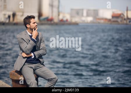 Comment puis-je améliorer cette entreprise. Un beau jeune homme d'affaires assis seul près du port et regardant contemplatif pendant la journée. Banque D'Images