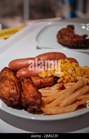 A vertical closeup of corn, french fries, chicken, and sausages, unhealthy fast food on a white plate Stock Photo