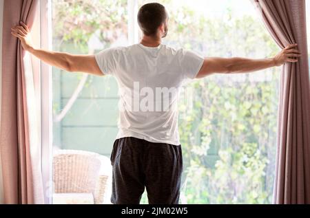 J'aime ouvrir les rideaux à un jour ensoleillé. Un jeune homme qui ouvre le rideau le matin à un jour ensoleillé. Banque D'Images