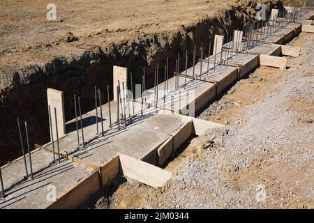 Tranchée sur site de construction avec semelles en béton armé pour supporter le mur de fondation d'un bâtiment. Banque D'Images