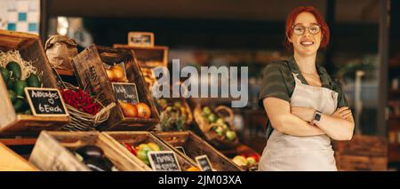 Heureux propriétaire de supermarché souriant à la caméra tout en se tenant dans la section des produits frais de son épicerie. Une jeune femme qui a réussi à courir une petite Banque D'Images