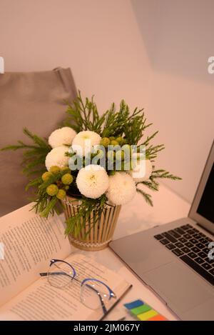 A vertical shot of a decorative vase with a green-white bouquet on a working desk Stock Photo