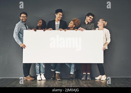 Un espace publicitaire d'un groupe diversifié de jeunes gens d'affaires professionnels heureux et souriants tenant un panneau blanc vierge. Une équipe multiraciale d'hommes et Banque D'Images