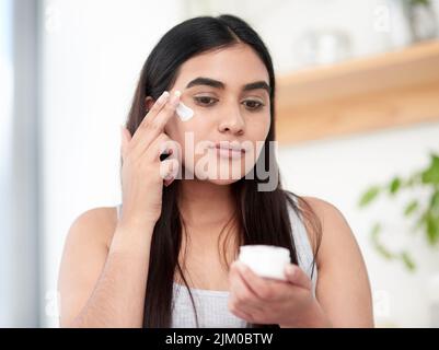La consistance est la clé de la peau rayonnante et brillante. Une magnifique jeune femme qui applique soigneusement son hydratant. Banque D'Images