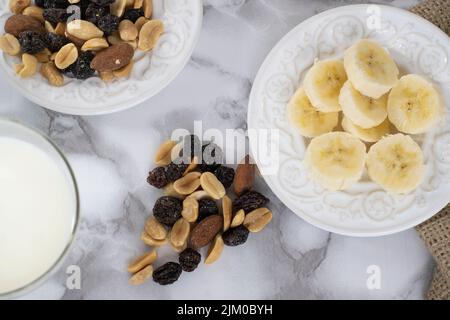 Vue de dessus d'un mélange de pistes sur une assiette blanche avec des tranches de bananes et du lait sur une table en marbre Banque D'Images