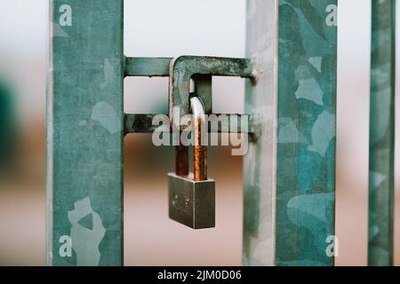 A closeup of an old rusty padlock on a green metallic gate Stock Photo