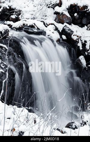 Un plan vertical d'une cascade qui coule le long des rochers couverts de neige en hiver Banque D'Images