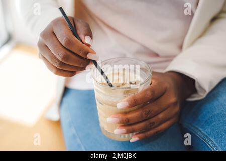 Vue rapprochée des mains de la femme africaine mélangeant la boisson avec la paille avant de la boire. Concept de style de vie Banque D'Images