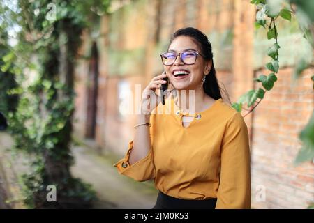 Une jeune brunette latino-américaine parle au téléphone en portant des lunettes souriantes Banque D'Images