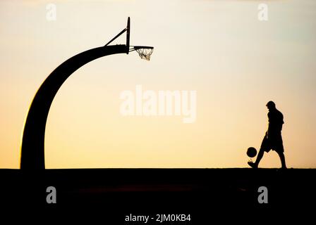 Le panier de basket-ball et la silhouette de l'homme avec une balle contre le coucher du soleil. Banque D'Images
