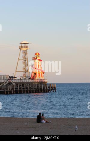 Une vue de couple assis sur la plage en arrière-plan de Helter squelette sur la jetée victorienne à Bournemouth Banque D'Images