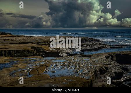 ROCKY COASTLINE IN LA JOLLA CALIFORNIA WITH TIDE POOLS AND WAVES FROM THE PACIFIC OCEAN AND STORM CLOUDS Stock Photo