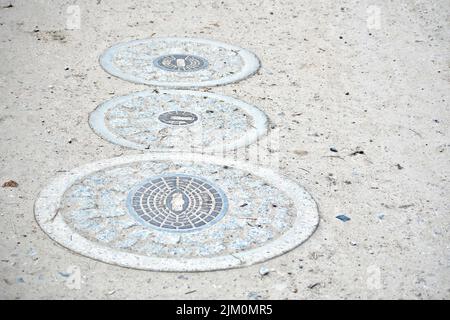 Three manhole covers on a gravel road in a row Stock Photo