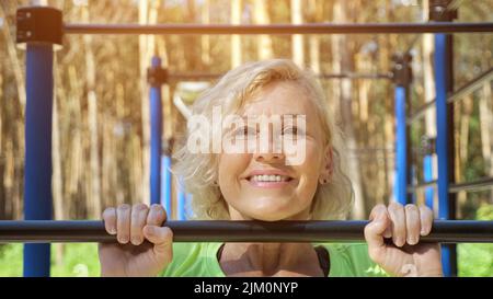 Une femme mûre fait des pull-ups souriant sur le terrain de sport gros plan Banque D'Images