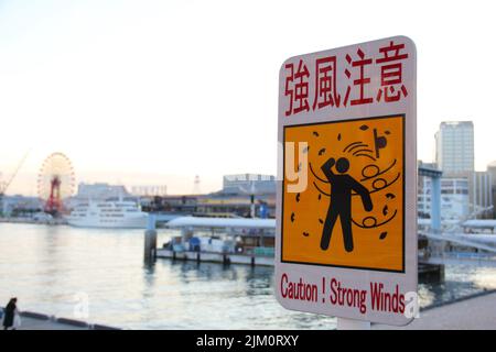 A sign in Japanese and English warns of strong winds in the port of Kobe Stock Photo