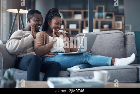 C'est tellement bon de vous voir tous. Un jeune couple heureux assis ensemble sur leur canapé et utilisant un ordinateur portable pour un chat vidéo. Banque D'Images
