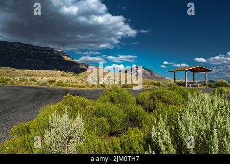 A gazebo on the side of the road in the middle of a green field with mountains in the background Stock Photo