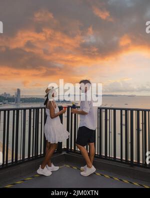 Deux hommes et femmes sur un bar sur le toit à Pattaya, vue de la terrasse du Hilton Sky Bar au coucher du soleil. Pattaya bar sur le toit Thaïlande. Banque D'Images