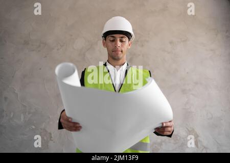 Jeune architecte musulman homme portant un casque d'entrepreneur tenant le projet Blueprints papier plan sur la construction isolée de fond, heureux avec grand sourire Banque D'Images