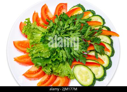 Tranches de tomates, concombres, poivron rouge et garni de persil et de laitue. Assiette de légumes frais. Isoler. Banque D'Images