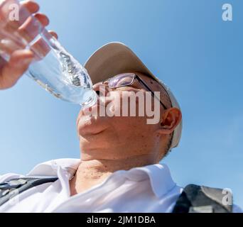 Un homme âgé boit beaucoup d'eau lors d'une journée d'été record pour éviter la déshydratation pendant ses heures de sortie. Banque D'Images