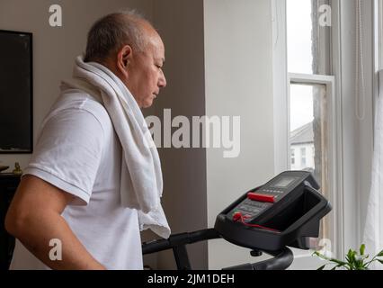 Un homme âgé essayant de garder la forme en train de travailler sur un tapis roulant à la maison. Banque D'Images