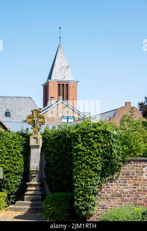 Deutschland, NRW, Kreis Düren, Vettweiß, Wegekreuz au18. JH.Am Marktplatz, dahinter der Turm der katholischen Pfarrkirche Sankt Gereon Banque D'Images