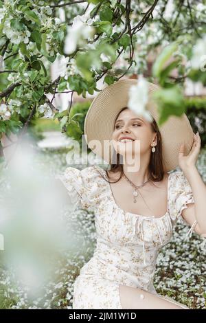 Une belle femme aux cheveux longs marche au printemps dans le parc de pommiers en fleurs. Banque D'Images