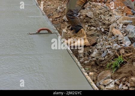 Le travailleur tient une truelle en acier et lisse le plâtrage sur le béton fraîchement coulé qui est humide Banque D'Images